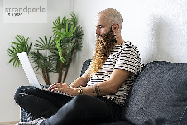 Hipster  der zu Hause auf der Couch sitzt und einen Laptop benutzt