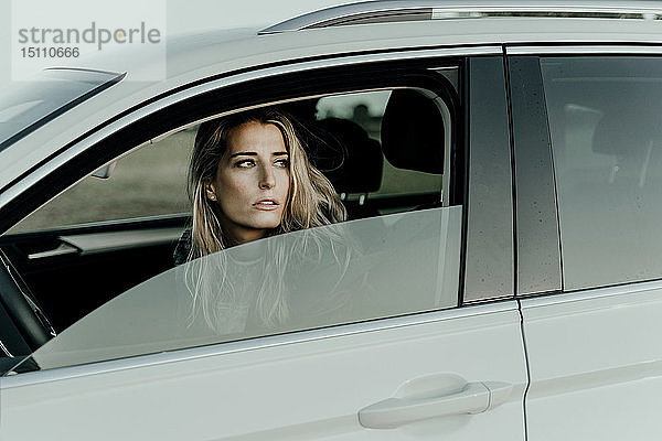 Blonde Frau in weißem Auto  die aus dem Fenster schaut