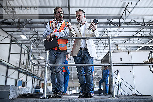Nachdenklicher Mann und Geschäftsmann mit Handy im Gespräch in der Industriehalle