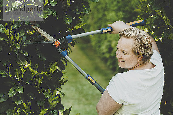 Eine Frau schneidet die Sträucher mit einer großen Gartenschere