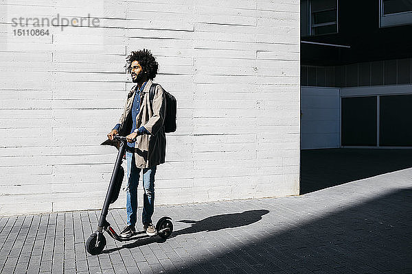 Mann mit Rucksack auf E-Scooter stehend