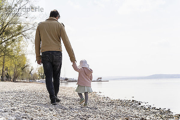 Deutschland  Bayern  Herrsching  Vater und Tochter beim Spaziergang am Kiesstrand am Seeufer