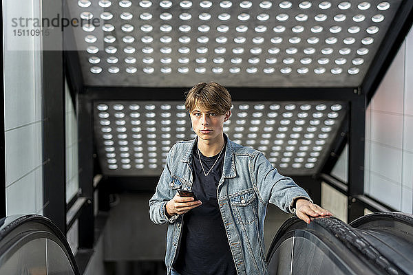 Porträt eines jungen Mannes mit Handy auf der Rolltreppe