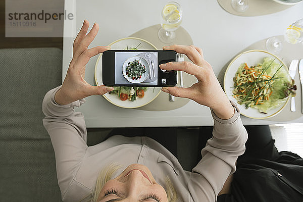 Junge Frau macht ein Handyfoto von einem Salat in einem Restaurant