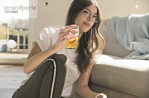 Junge Frau sitzt zu Hause mit einem Getränk auf dem Boden