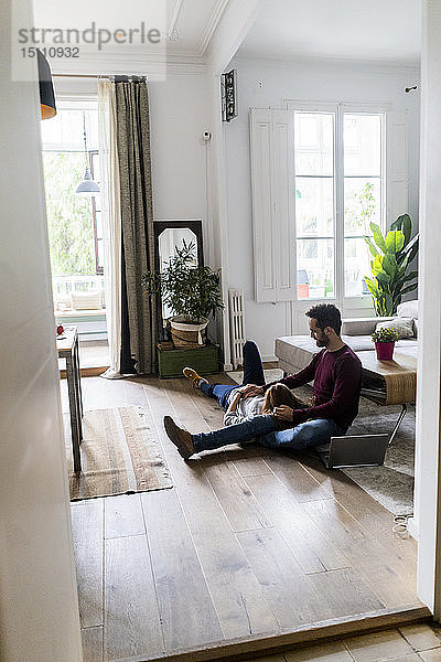 Zärtliches Paar mit Laptop  das sich zu Hause auf dem Boden entspannt