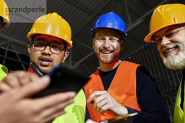 Glückliche Arbeiter im Fabriklager sprechen und benutzen Tabletten