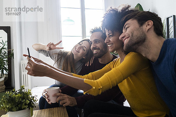 Vier glückliche Freunde sitzen auf der Couch und machen ein Selfie