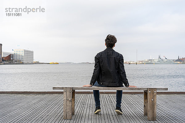 Dänemark  Kopenhagen  Rückansicht eines jungen Mannes  der auf einer Bank am Wasser sitzt