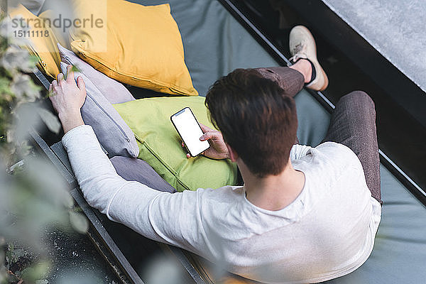 Draufsicht eines jungen Mannes  der auf einer Couch sitzt und ein Mobiltelefon benutzt