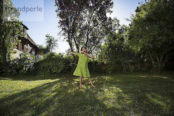 Mädchen mit Kopfhörern und Smartphone singt und tanzt im Garten