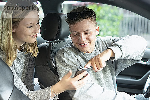 Lächelndes junges Paar im Auto  das auf sein Handy schaut