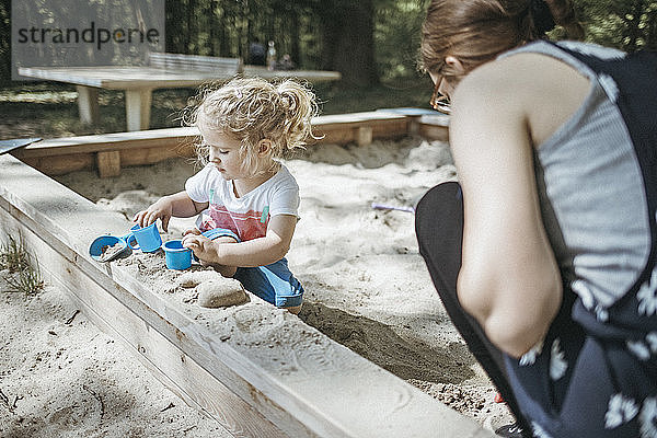 Mutter spielt mit kleiner Tochter im Sandkasten auf einem Spielplatz