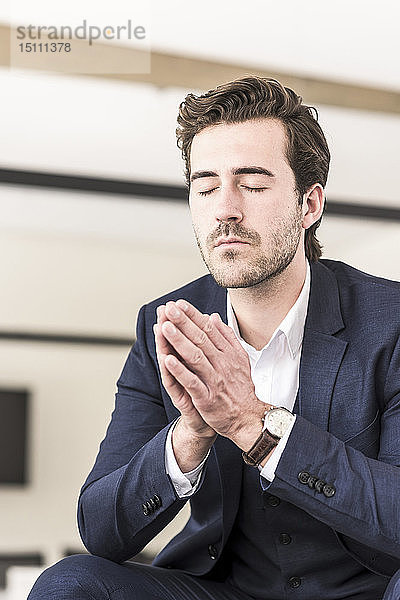 Junger Geschäftsmann betet mit geschlossenen Augen