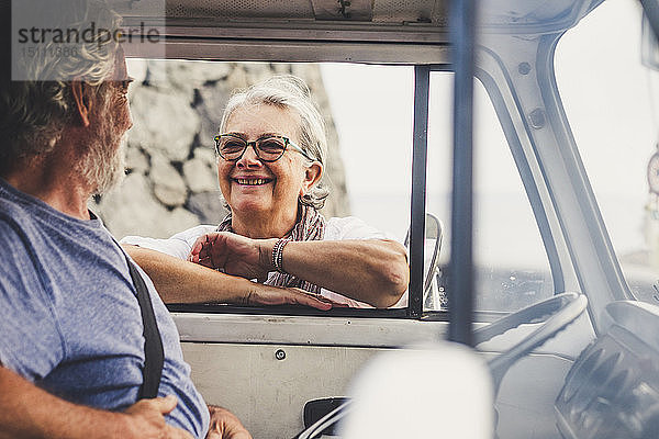 Älteres Ehepaar reist in einem Oldtimer-Van  macht eine Pause am Meer  unterhält