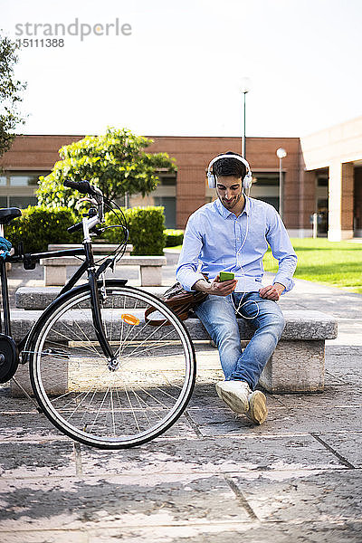 Junger Mann mit Fahrrad  der ein Smartphone benutzt und Musik hört