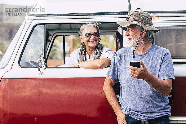 Älteres Ehepaar reist in einem Oldtimer-Van und benutzt ein Smartphone