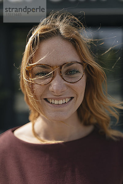 Porträt einer glücklichen jungen Frau mit Brille und windgepeitschtem Haar