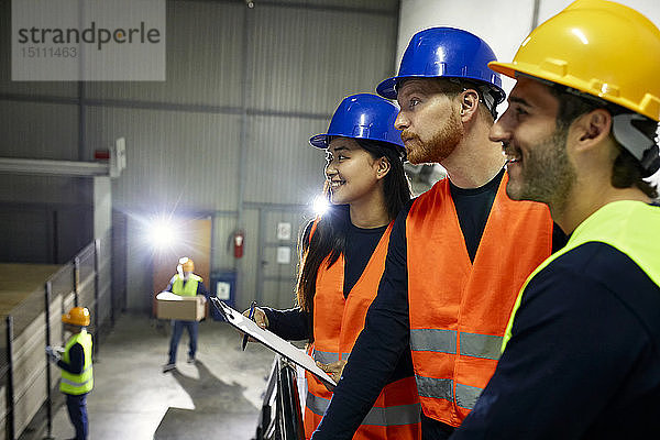 Zwei Männer und eine lächelnde Frau in reflektierenden Westen in der Fabrik