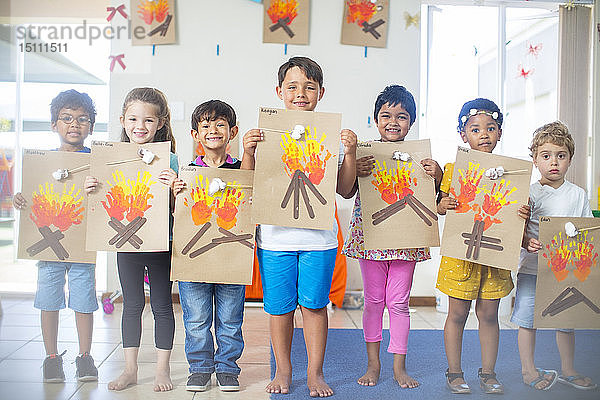 Porträt von lächelnden Kindern  die Bilder von Feuer im Kindergarten präsentieren