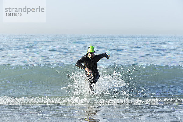 Triathlet im Neoprenanzug läuft aus dem Meer