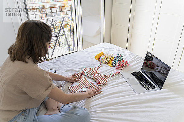 Junge Frau mit Laptop legt Bikini aufs Bett