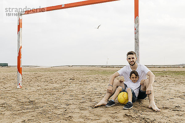 Mann und Junge ruhen sich nach Fußballspiel am Strand aus