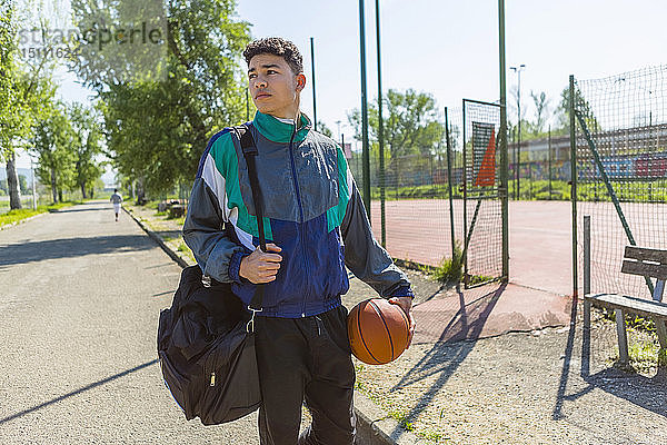 Junger Mann mit Basketball am Basketballplatz