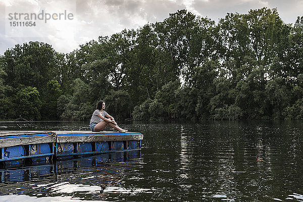 Entspannte Frau sitzt auf einem Steg an einem abgelegenen See