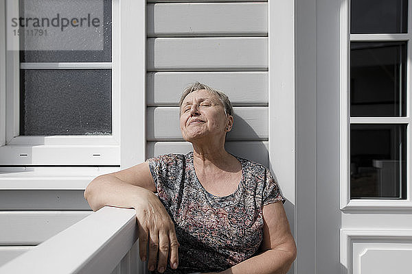 Entspannte ältere Frau sitzt auf der Veranda im Sonnenschein