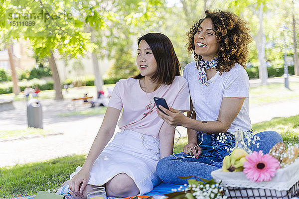 Zwei Frauen mit Handy und Kopfhörern im Park