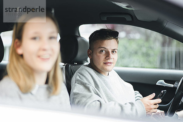 Porträt eines jungen Mannes mit Smartphone am Fahrersitz