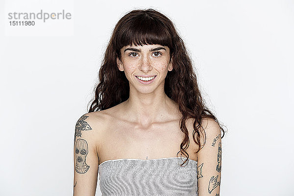 Porträt einer lächelnden jungen Frau mit Sommersprossen und Tätowierungen auf den Oberarmen