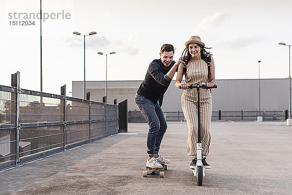 Junger Mann und Frau fahren auf Longboard und Elektroroller auf dem Parkdeck