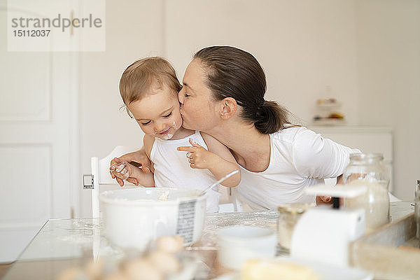 Mutter küsst kleine Tochter beim gemeinsamen Kuchenbacken in der heimischen Küche