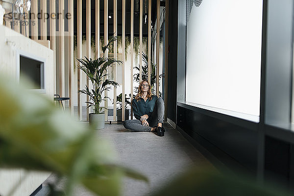 Geschäftsfrau  die in einem modernen Büro auf dem Boden sitzt