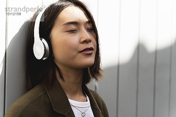 Entspannte junge Frau mit geschlossenen Augen  die mit Kopfhörern Musik hört