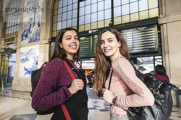 Porträt von zwei lächelnden jungen Frauen mit Rucksäcken vor dem Bahnhofsgebäude  Porto  Portugal