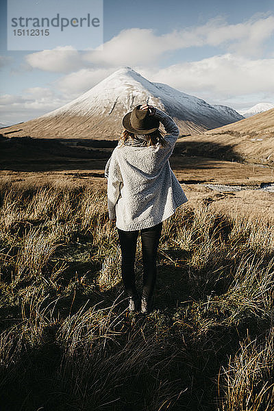 Großbritannien  Schottland  Loch Lomond und der Trossachs-Nationalpark  Rückansicht einer jungen Frau  die in einer ländlichen Landschaft steht und auf einen Berg schaut
