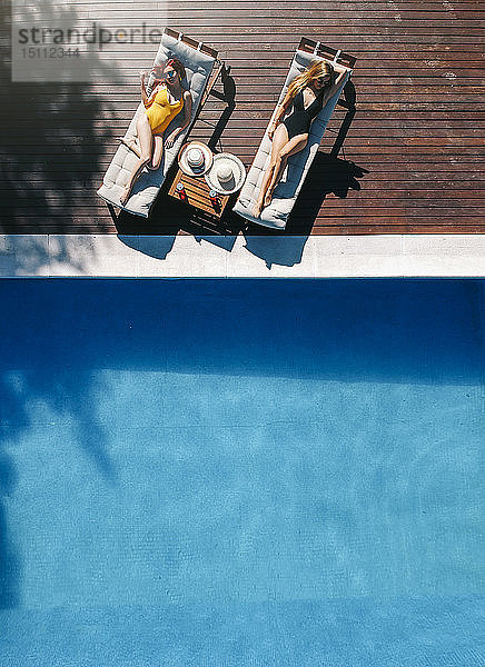 Zwei schöne Frauen sonnen sich auf einer Terrasse neben dem Pool