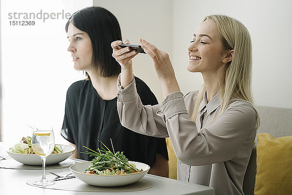 Junge Frau beim Fotografieren eines Salats in einem Restaurant mit dem Handy