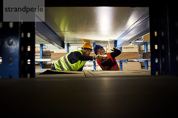 Zwei Arbeiter mit Taschenlampe suchen etwas im Fabriklager