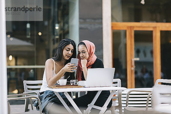 Zwei Freunde sitzen mit dem Handy in einem Straßencafé zusammen