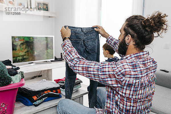 Vater faltet Wäsche im Wohnzimmer  während sein Sohn ein Computerspiel spielt