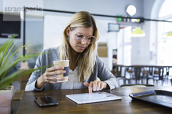 Junge Frau  die mit ihrem digitalen Tablet arbeitet  während sie im Café Kaffee trinkt
