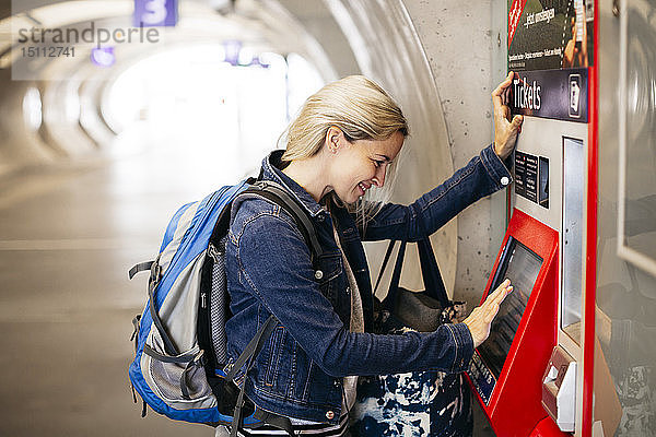 Lächelnde Frau am Fahrkartenautomaten am Bahnhof
