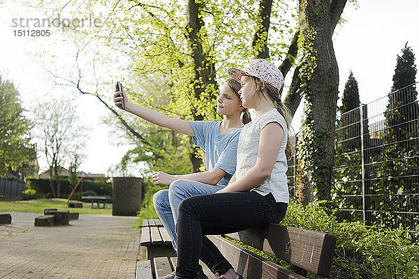 Zwei Mädchen sitzen auf einer Parkbank und machen ein Selfie