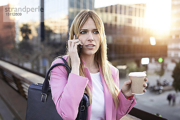 Junge Geschäftsfrau benutzt Smartphone und hält Kaffee zum Mitnehmen