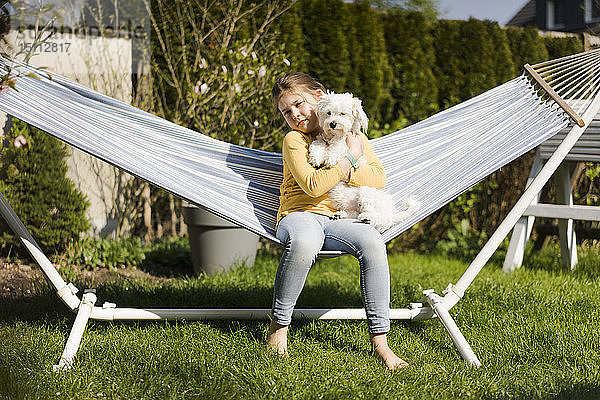 Porträt eines Mädchens mit Hund in Hängematte im Garten