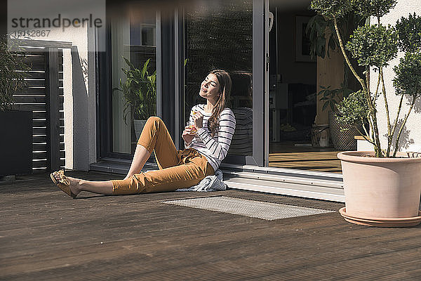 Junge Frau sitzt zu Hause auf der Terrasse und genießt den Sonnenschein